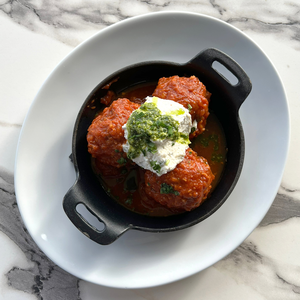 Photo of ZIMI Italian's homemade meatballs in red sauce, topped with cream and pesto.