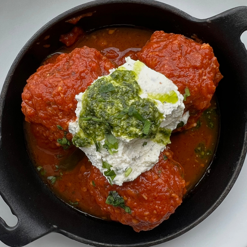 Photo of ZIMI Italian meatballs in red sauce topped with cream and pesto.